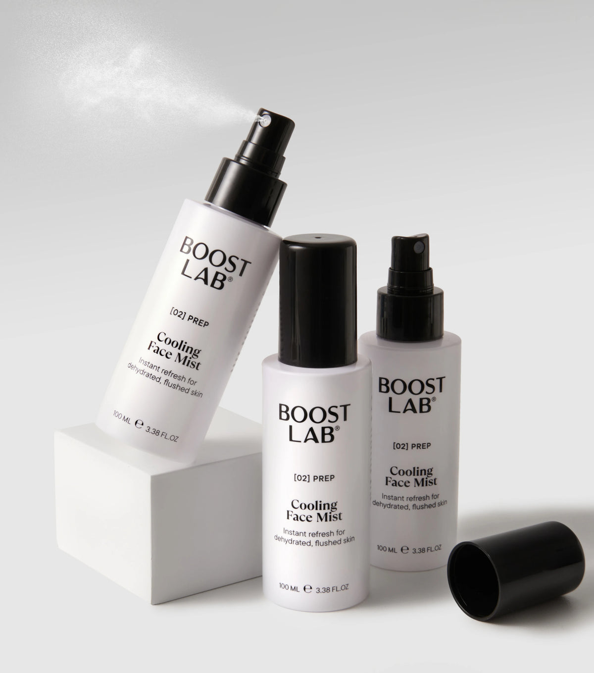 Boost Lab Cooling Face Mist spraying from a white plinth, with a second bottle and cap beside it