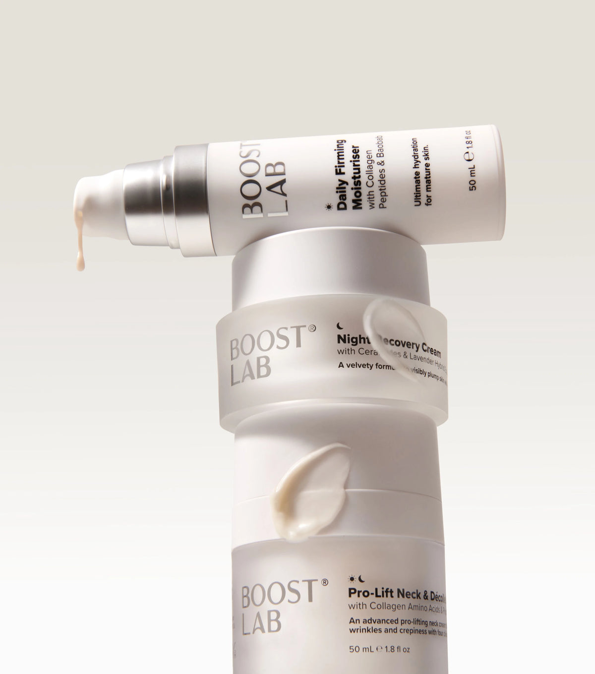 Three white Boost Lab skincare bottles stacked vertically with cream smeared across the front, photographed on a clean light gray background.